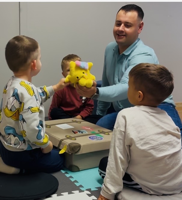 Paweł prowadzi zajęcia z dziećmi, wykorzystując żółtą maskotkę Kiki.